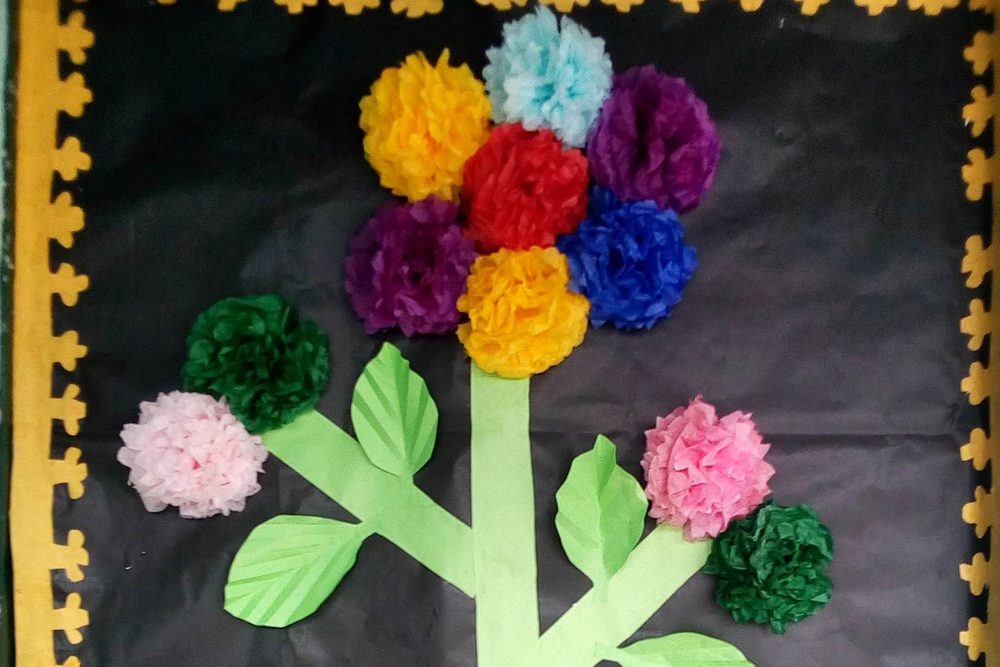 Pompones de papel crepé de colores formando las flores de un árbol en un mural