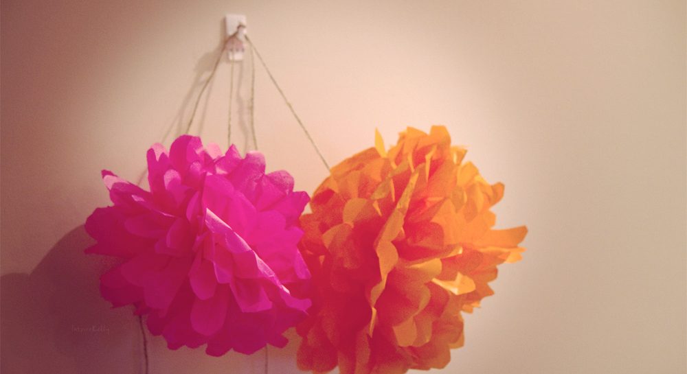 Pompones de papel de seda de colores colgando de una pared como guirnalda